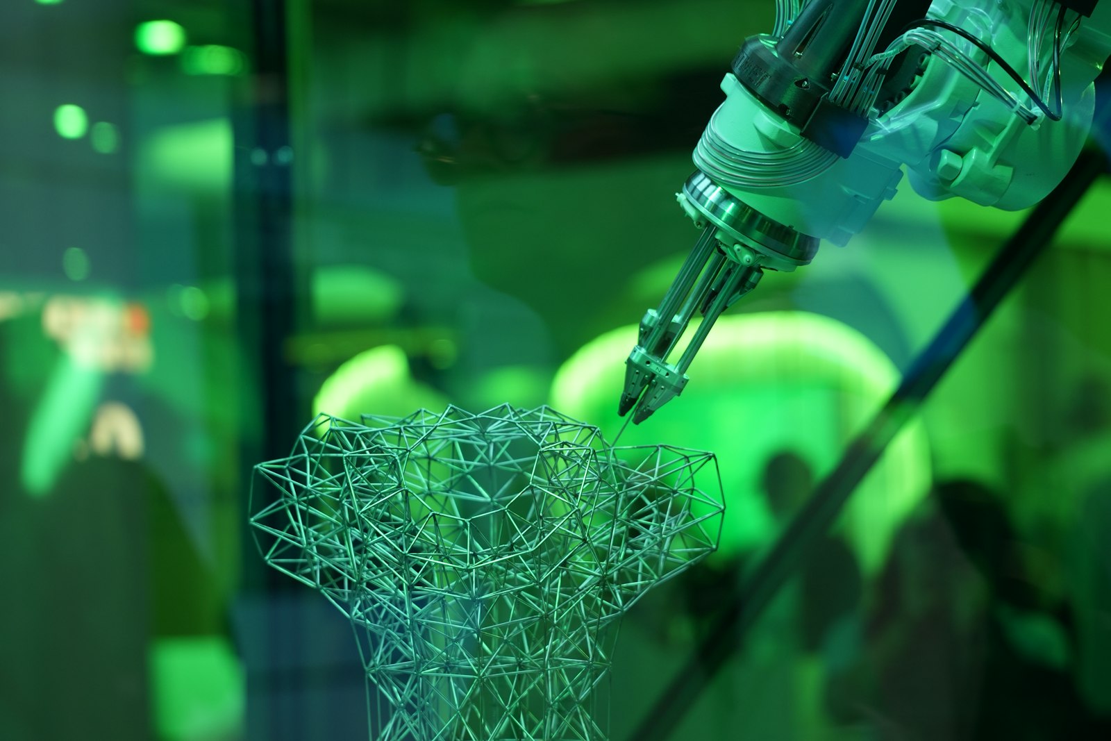 A robotic arm with a three-finger gripper assembling a lattice of thin metal struts under green light