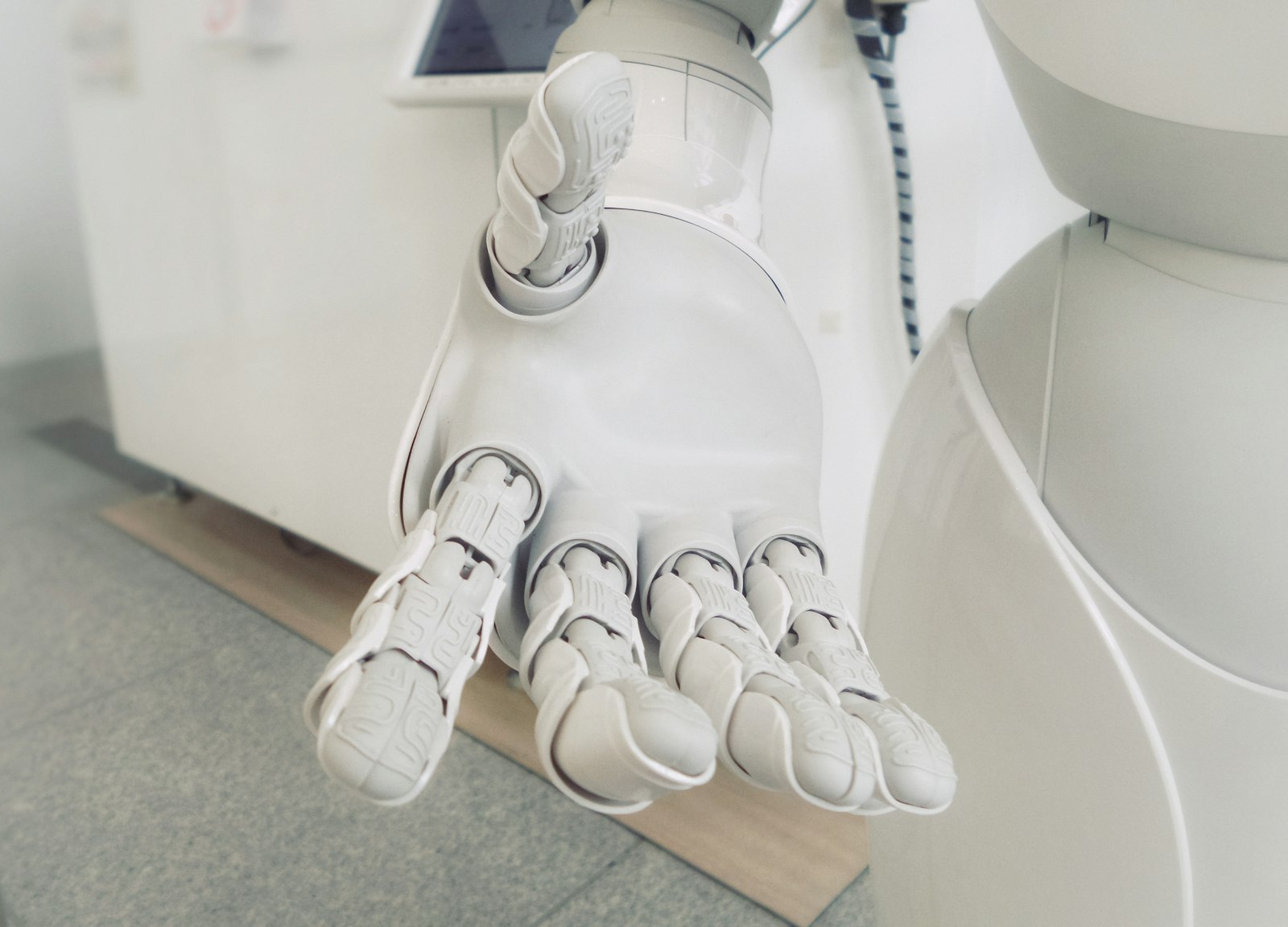 Close-up of a white humanoid robot's hand held open, palm up, with jointed fingers, in a bright room