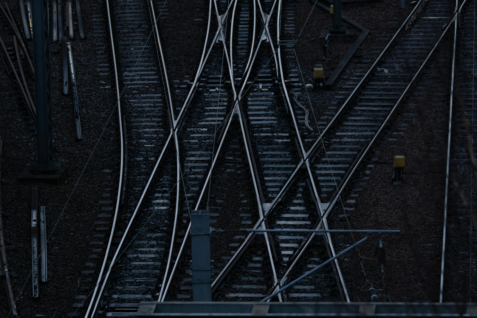 Overhead view of a rail yard at dusk where several steel tracks cross and branch through a series of switches