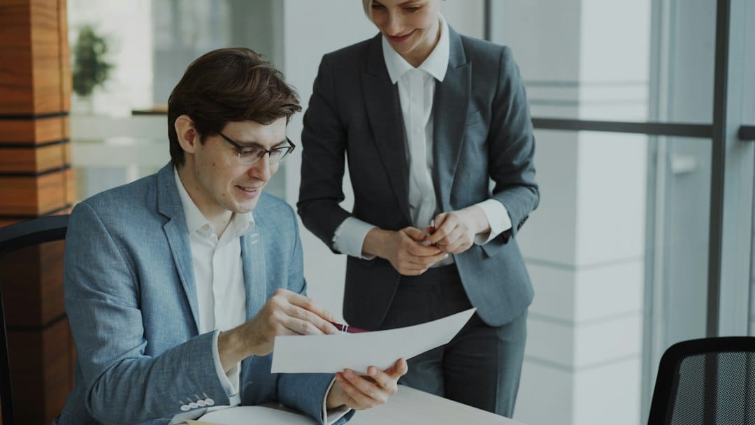 Two colleagues in business clothes reviewing a printed document together in an office, representing a company drafting and approving its AI acceptable use policy