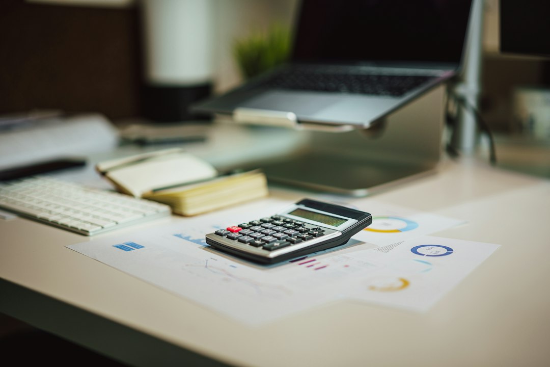 A calculator on printed financial statements beside a laptop and keyboard on an accountant's desk