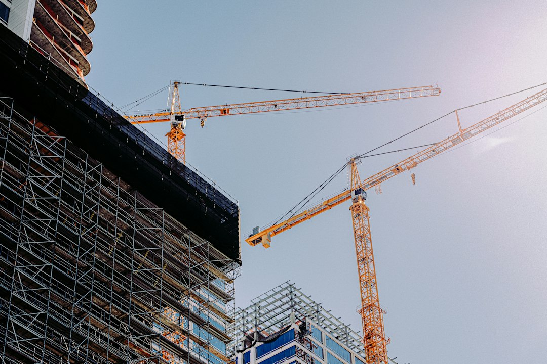Two tower cranes rising over a building under construction wrapped in scaffolding