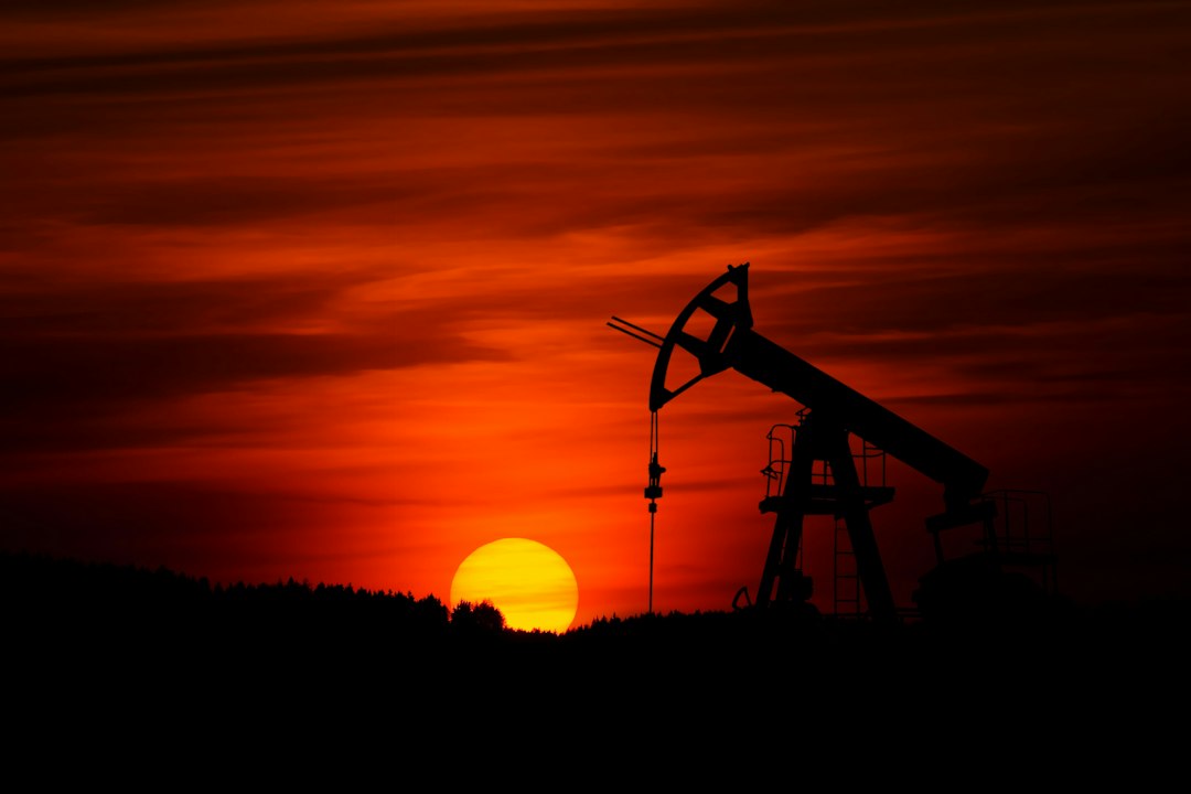 The silhouette of an oil pump jack against a red sunset