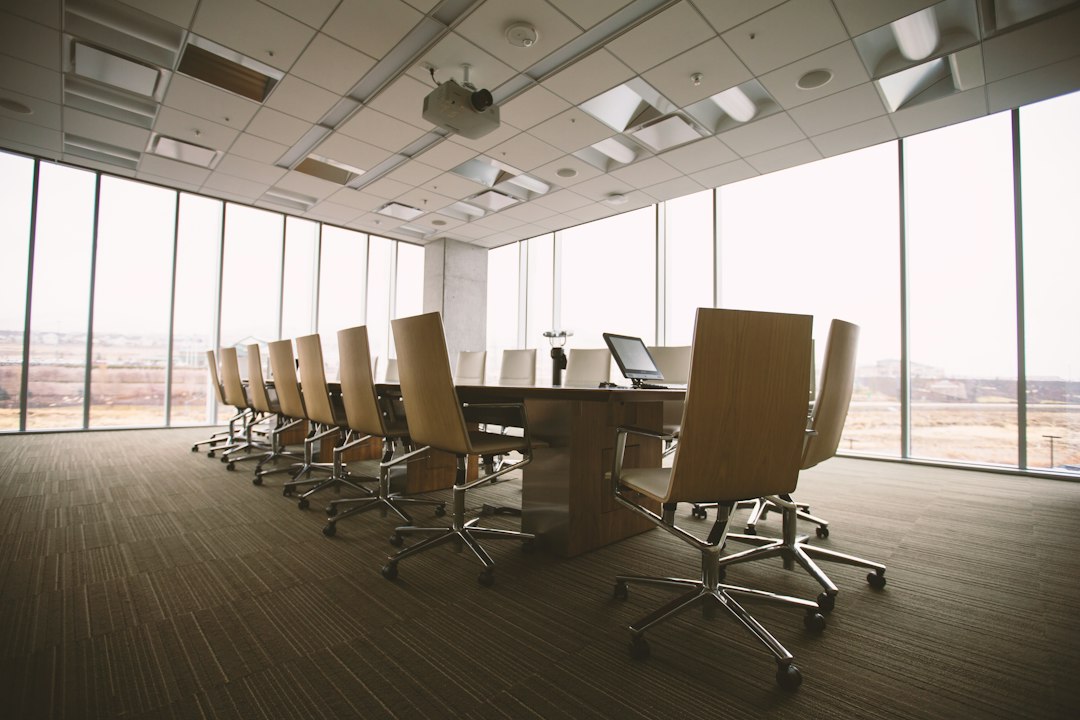 An empty conference room with a long wooden table and leather chairs in front of floor-to-ceiling windows, ready for an investment committee meeting