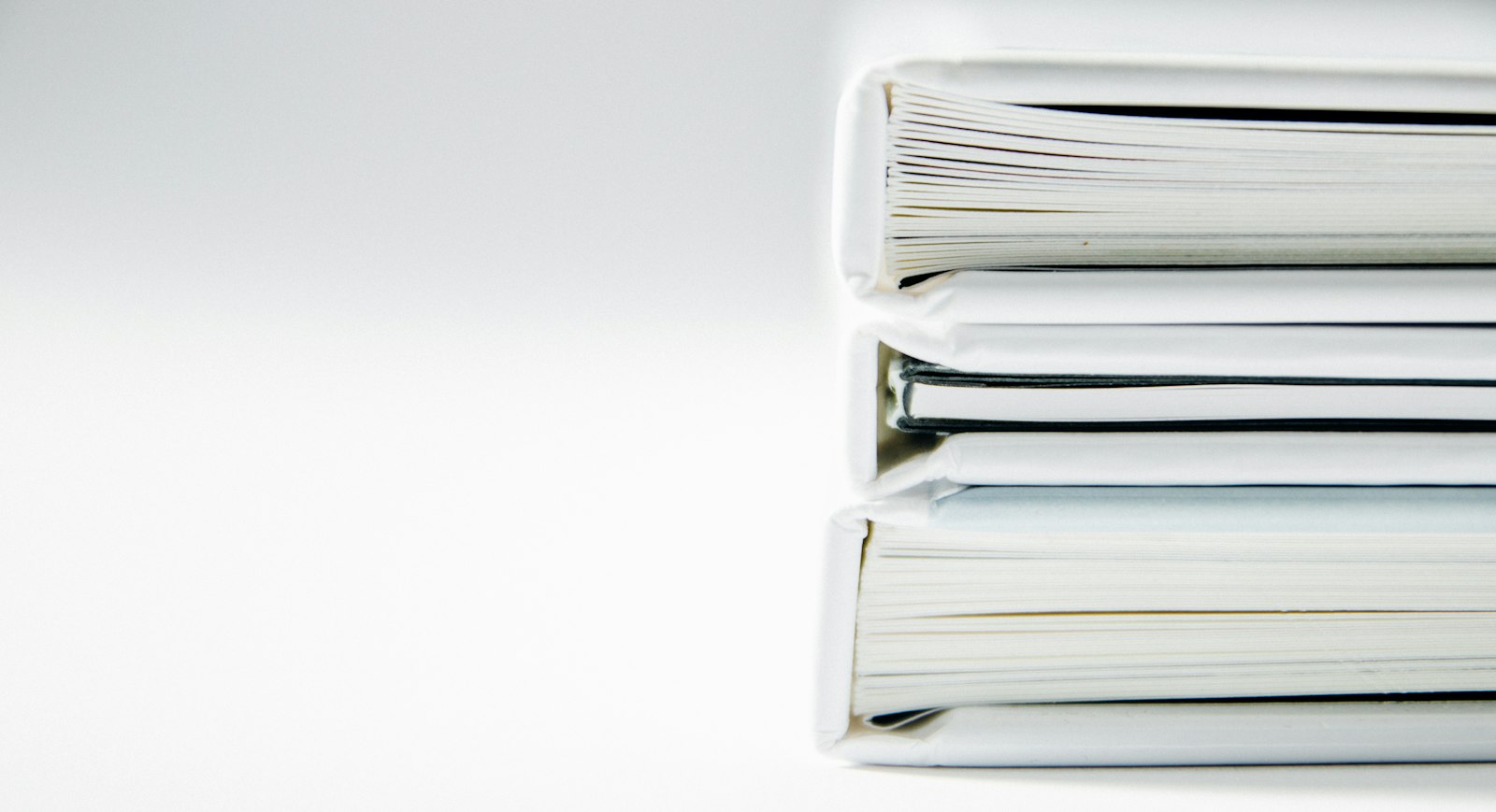 A stack of three thick white ring binders full of paper, photographed from the side against a plain white background