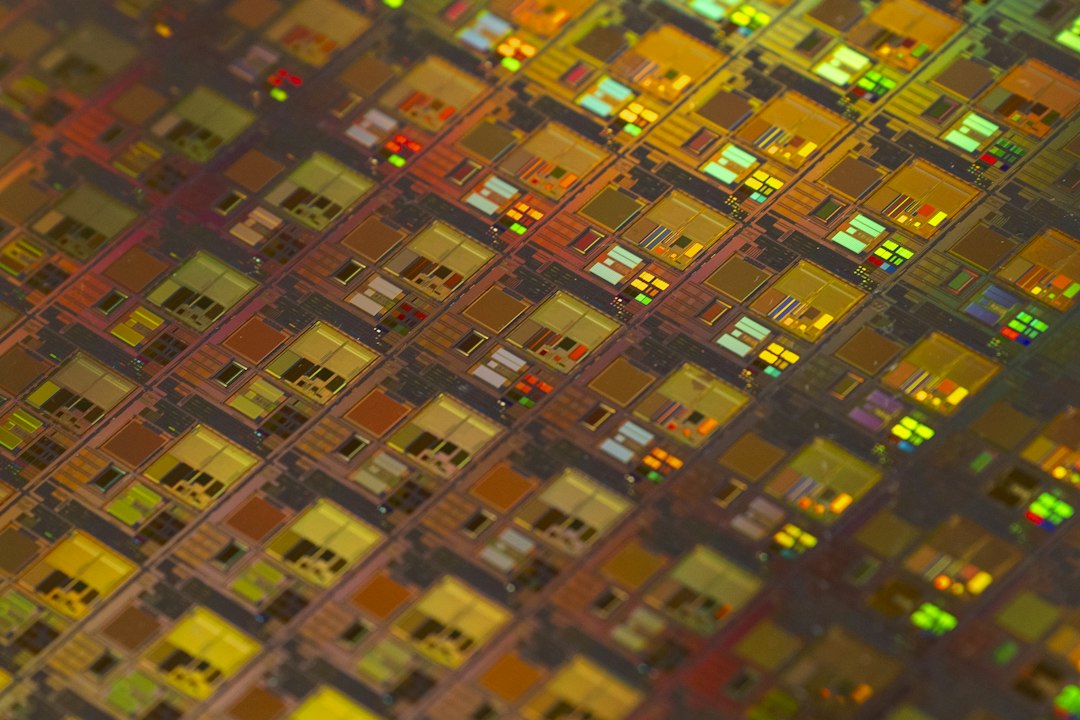 A close-up of a silicon wafer showing a grid of identical chip dies reflecting gold and green light