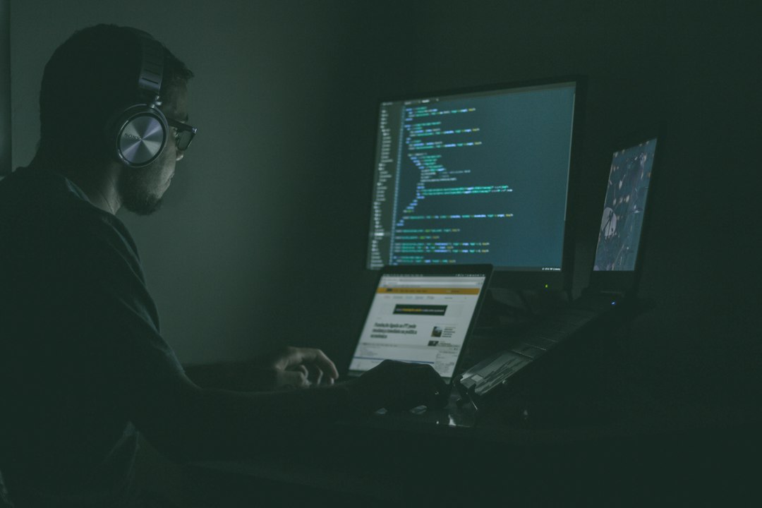 An engineer wearing headphones works late at a desk with code on two monitors, the kind of setting where an AI incident is triaged