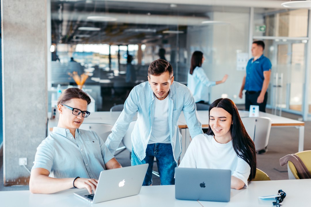 Three colleagues reviewing work on laptops in an open-plan office, representing relationship managers preparing client briefings with a private AI assistant that respects bank information barriers