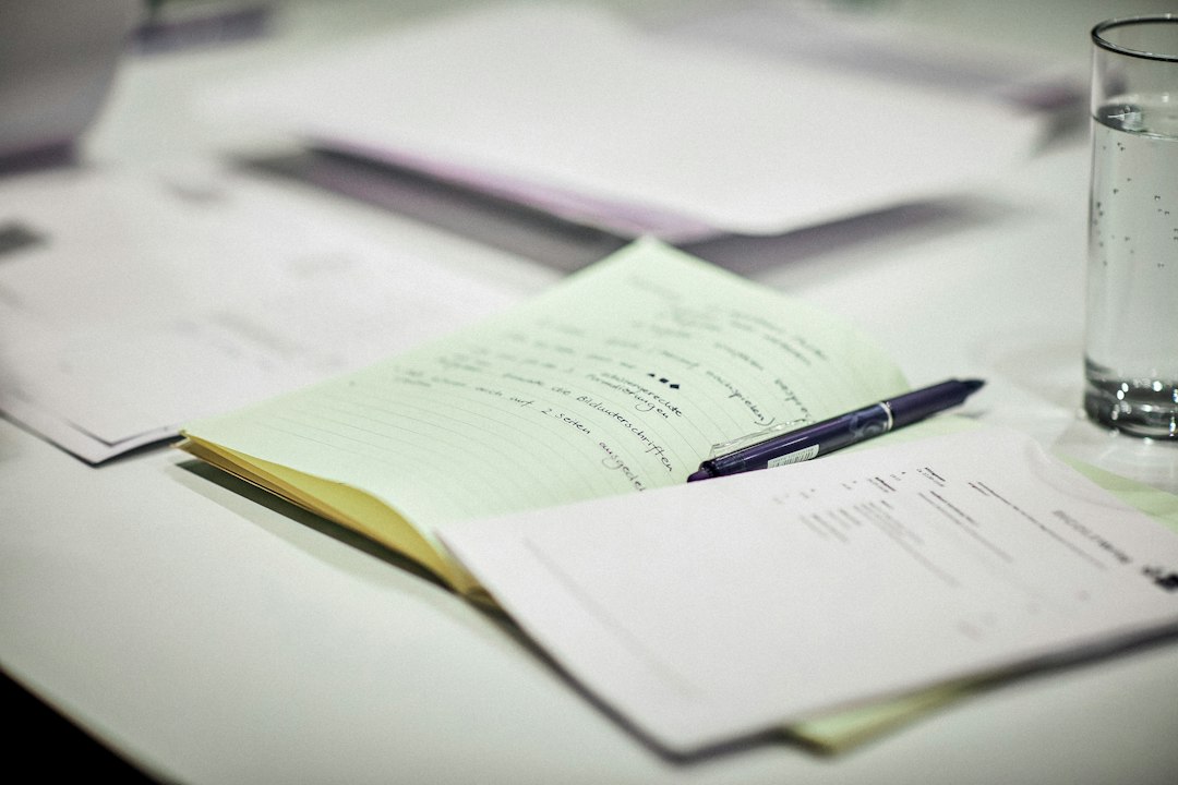 Loose pages of notes and a yellow legal pad with a pen beside a glass of water on a white table, the paperwork of a vendor security review