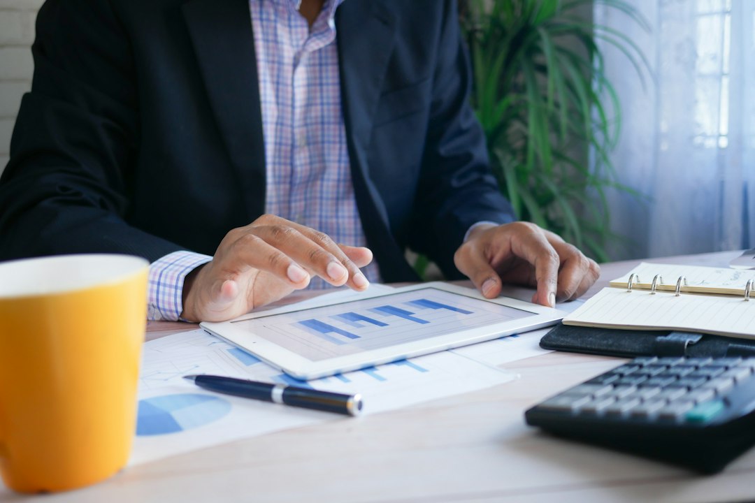 An analyst in a suit reviews bar charts on a tablet next to a calculator and printed financial reports