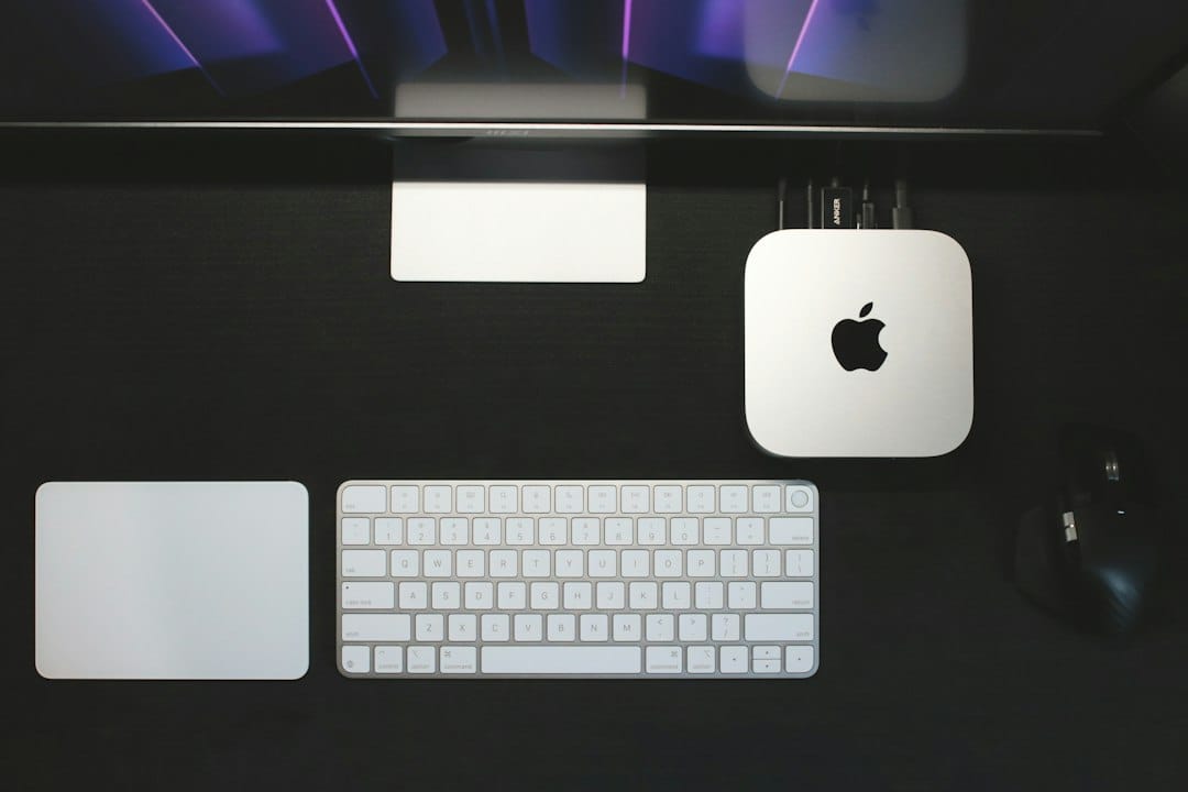 Top-down view of a Mac mini beside a keyboard and trackpad on a dark desk, the kind of compact Apple silicon machine people use to run local language models