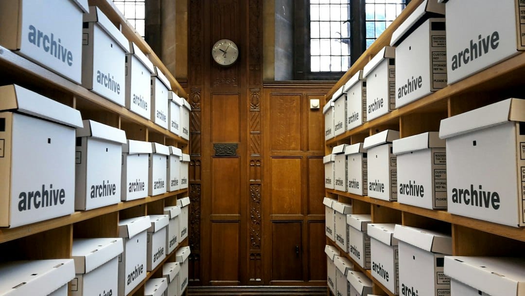 Rows of white archive boxes on wooden shelves in a records room, a picture of the document collections a retrieval-augmented generation system has to answer from