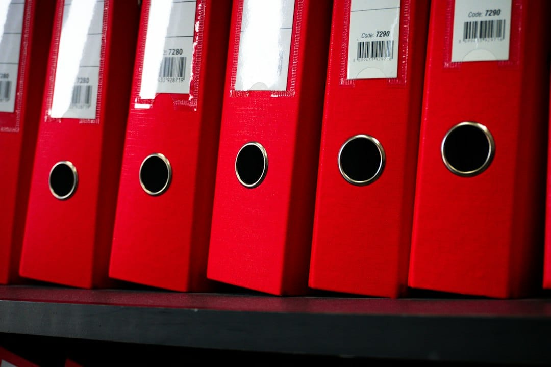 A row of red ring binders with barcode labels on an office shelf, a reminder of how much company knowledge an enterprise AI search tool has to index and keep behind the right permissions