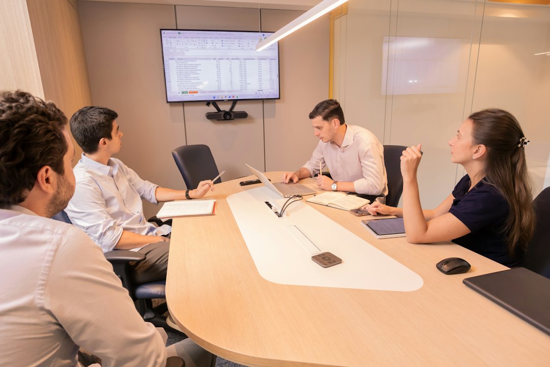 Four colleagues around a meeting-room table reviewing a spreadsheet on a wall screen, representing a compliance review of EU AI Act Article 50 transparency duties for enterprise AI assistants