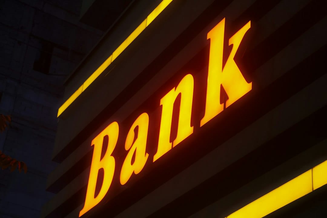 An illuminated yellow sign reading Bank on a dark building facade at night, standing in for the credit and insurance decisions that the EU AI Act classes as high-risk