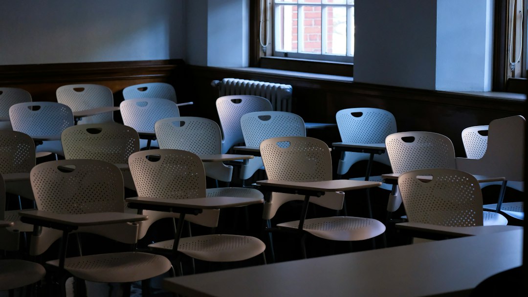 Rows of empty classroom chairs with fold-down writing tablets in a dim room, the setting for AI used in admissions, grading and exam proctoring