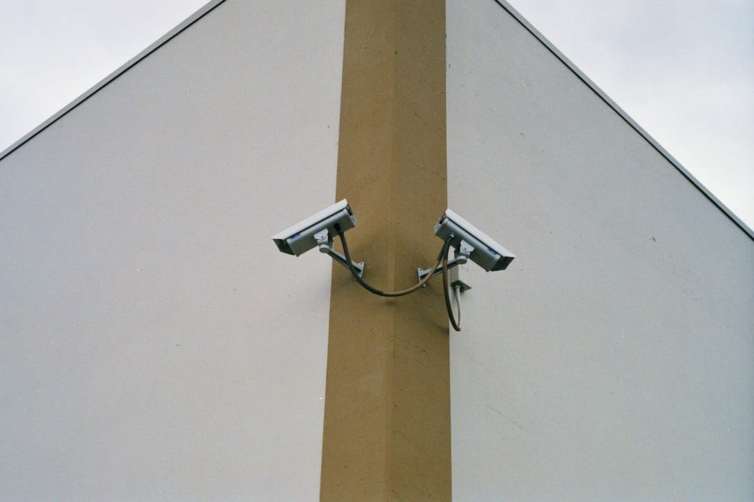 Two security cameras mounted on the corner of a pale building and pointing in opposite directions, a reminder that several EU AI Act Article 5 bans concern surveillance and biometric identification