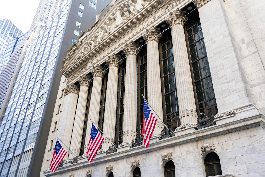 The New York Stock Exchange facade with American flags between its columns, framed by office towers in lower Manhattan