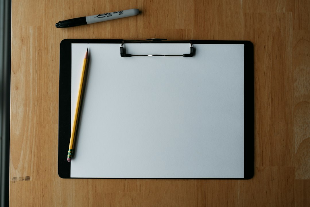 A blank clipboard with a pencil and a marker on a wooden desk, ready for an impact assessment template to be filled in