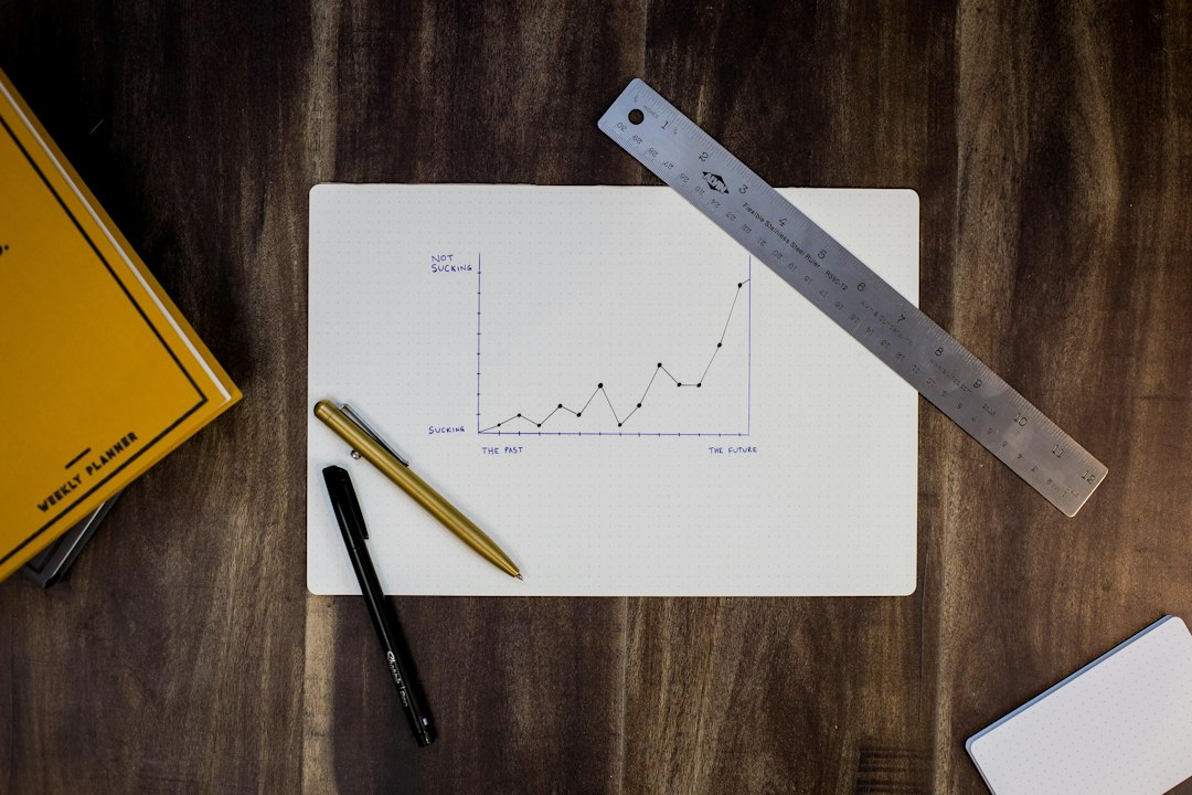 A hand-drawn rising line chart on paper with a steel ruler and two pens on a dark wooden desk, representing the budget planning behind an AI rollout
