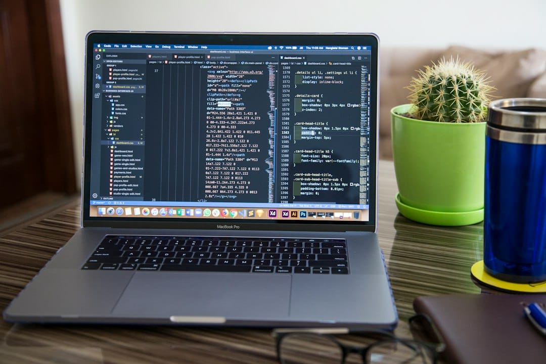 A laptop on a wooden desk with its screen split into several tiled terminal and editor panes, next to a potted cactus and a coffee cup