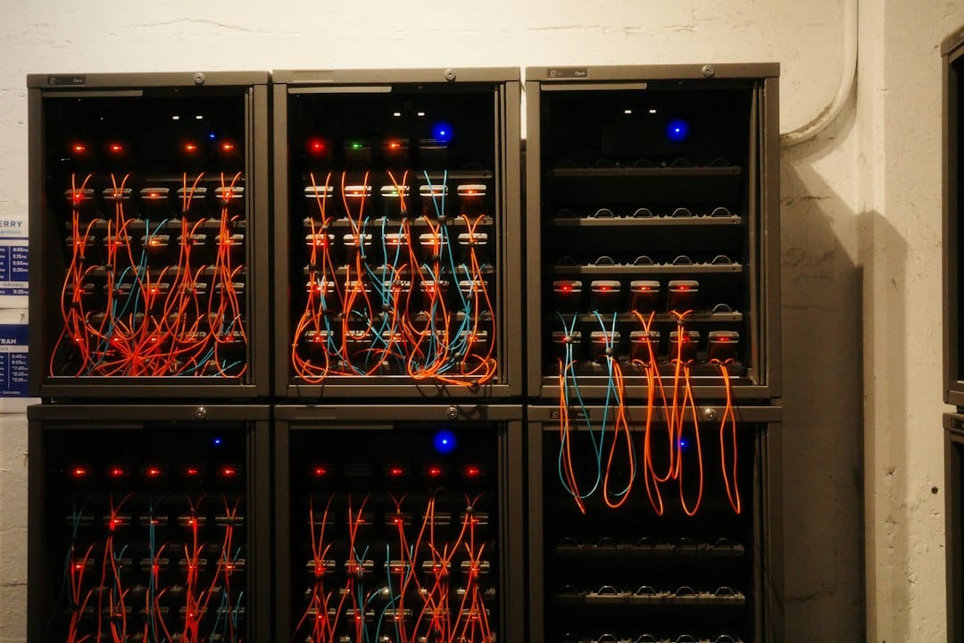 Six dark equipment cabinets in two rows against a whitewashed wall, each threaded with orange and blue cables and lit by status lights, like the GPU nodes of a small Kubernetes cluster wired into one system
