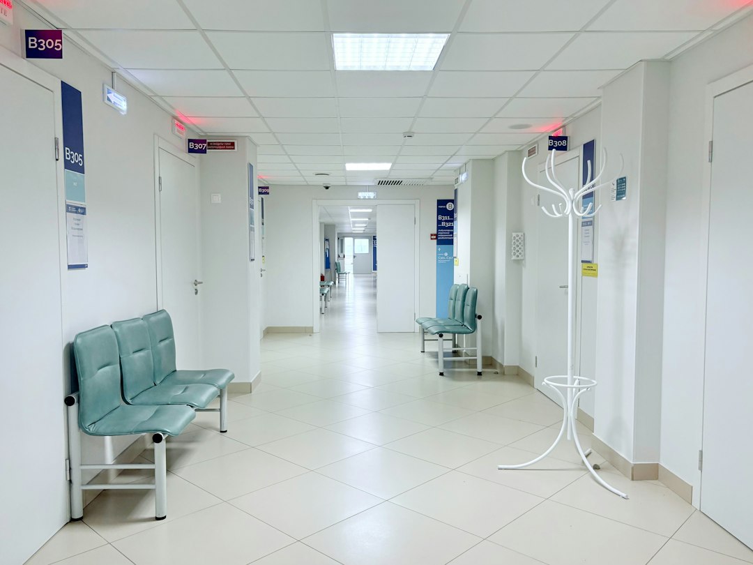 A bright, empty hospital corridor with teal waiting-room seats and closed doors, the setting where patient information has to stay protected