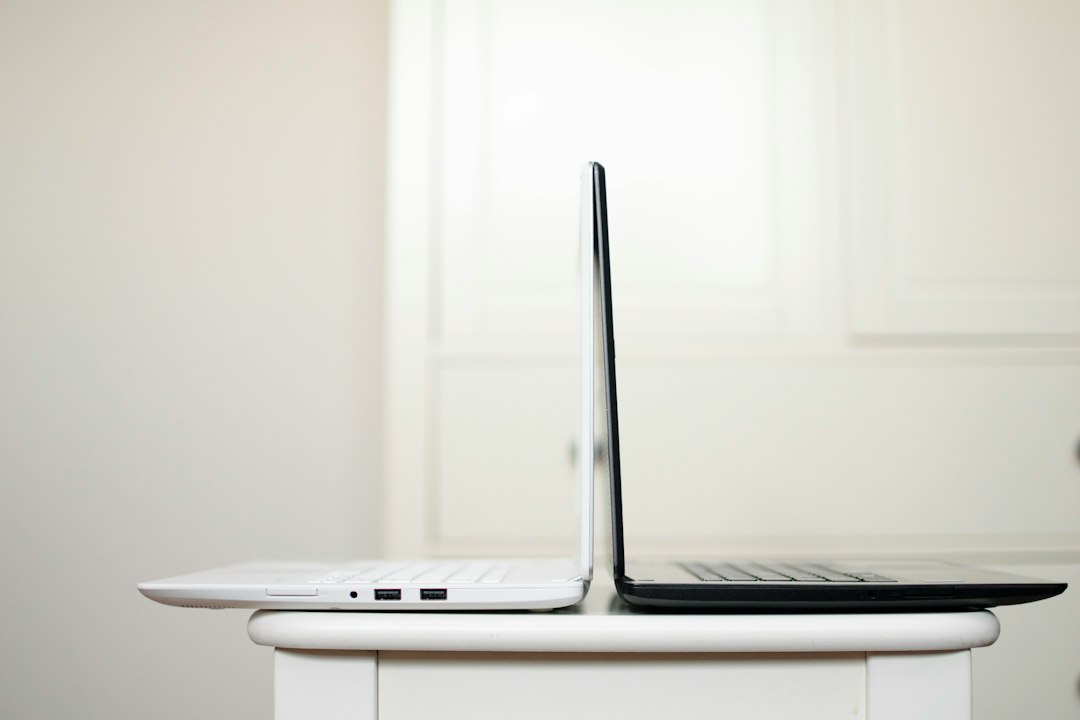 Two laptops, one white and one black, standing back to back on a small white table, a simple picture of comparing two desktop AI apps