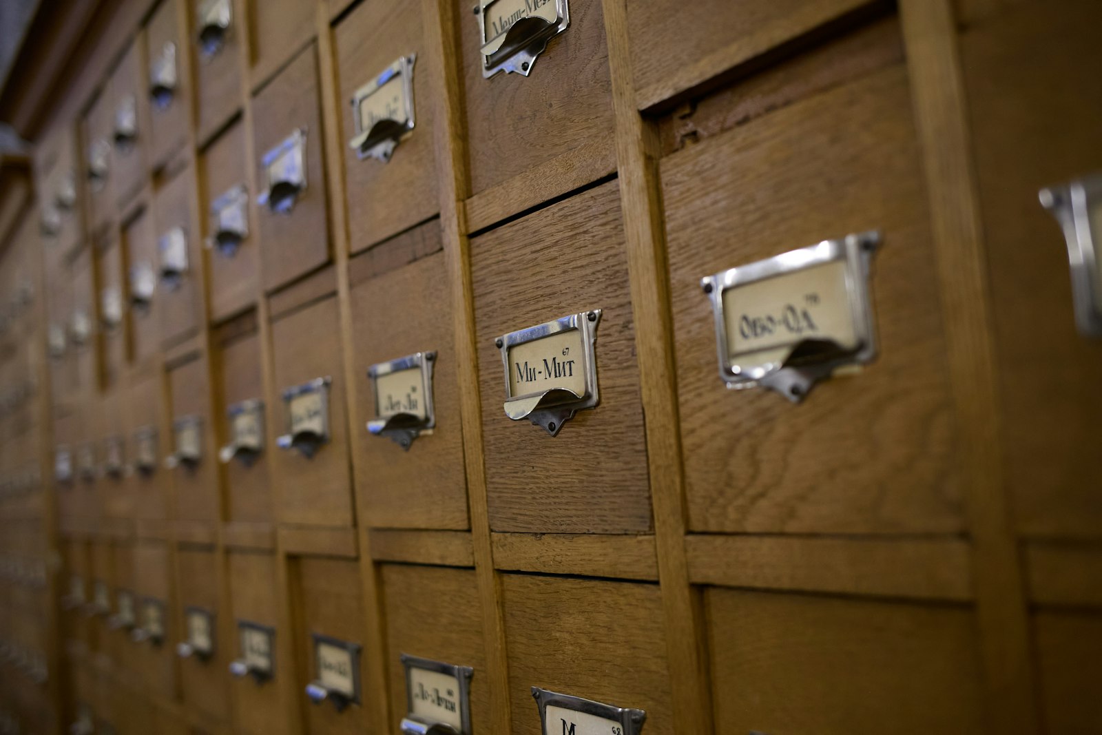 A wall of wooden library card catalogue drawers, each with a metal handle and a small label holder, receding at an angle