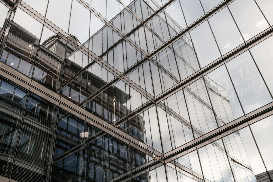 Looking up at a glass-walled office building that reflects a neighbouring tower, a setting for the per-user licences large organisations buy for Copilot