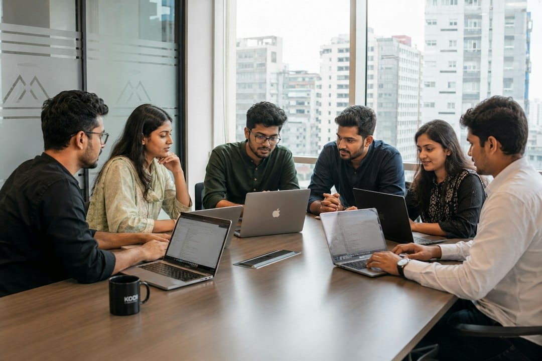Six colleagues working on laptops around a conference table in a high-rise office, the kind of group a shared, self-hosted chat interface has to serve with separate accounts and permissions