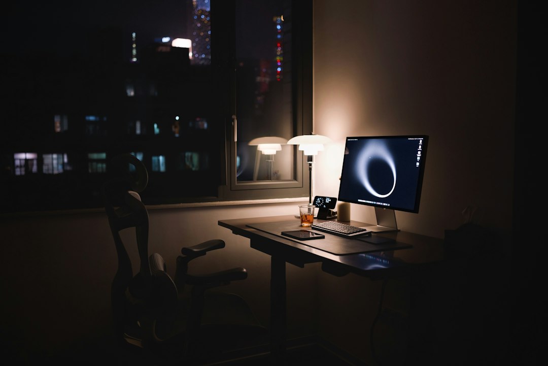 A desk by a night-time window lit by one lamp and a monitor, a quiet workstation for pointing a coding agent at a local model server